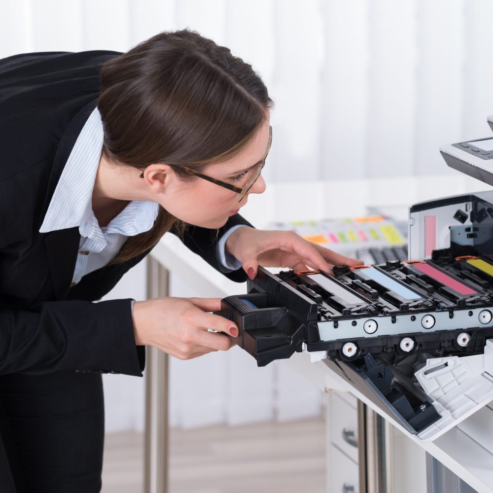 Young Businesswoman Fixing Copy Machine At Workplace